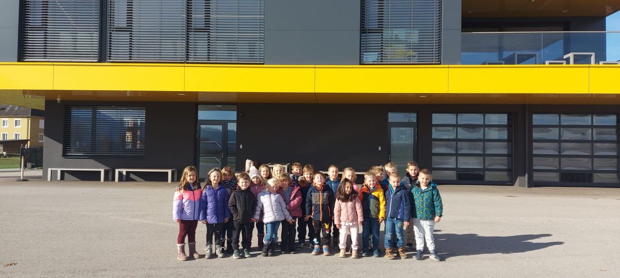 Eine Gruppe von Kindern in Winterkleidung steht vor einem Gebäude mit gelbem Dach und grauen Wänden. Sie posieren für ein Foto.