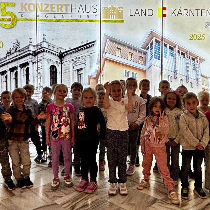 A group of children posing for a photo in front of a poster for Konzerthaus Klagenfurt in 2025.