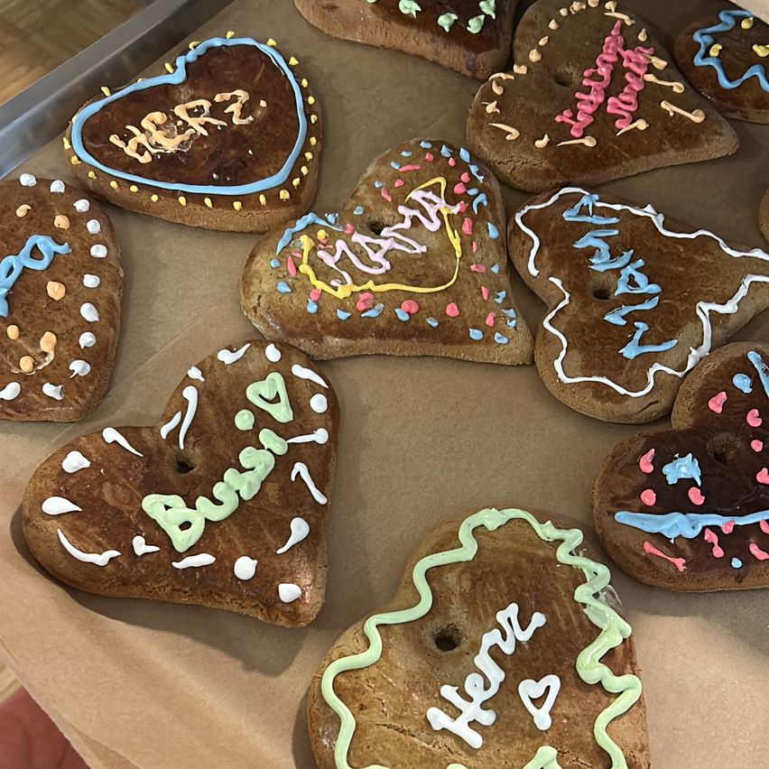 A tray with heart-shaped cookies, each decorated with different icing designs and words like 'Busing' and 'Here'. Some cookies have musical notes and birthday wishes.