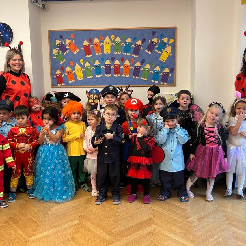 A group of children in costumes pose for a photo in a classroom with an adult woman and a clock.