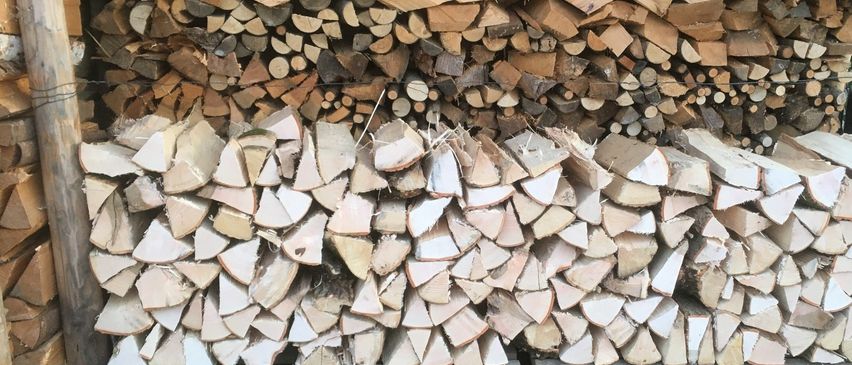 Ein großer Stapel Holzscheite ist ordentlich auf Holzpaletten gestapelt und in zwei Bereiche unterteilt. Ein Bereich besteht aus gemischten Holzarten, der andere hauptsächlich aus weißen und hellen Stücken.