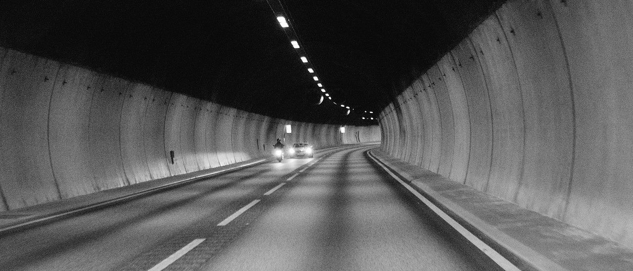 Ein Auto und ein Motorrad fahren bei Nacht durch einen schwach beleuchteten Tunnel.