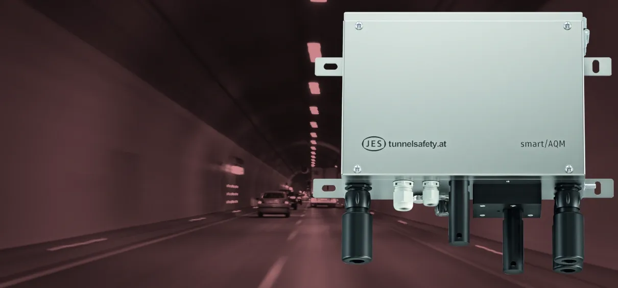 Ein Tunnelsicherheitsgerät mit der Marke 'JES' und dem Logo 'tunnelsafety.at', an einer Tunnelwand installiert, mit Autos im Hintergrund.