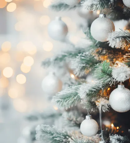 Ein Weihnachtsbaum ist mit silbernen Kugeln und einer Spur Schnee geschmückt, mit Bokeh-Lichtern im Hintergrund.