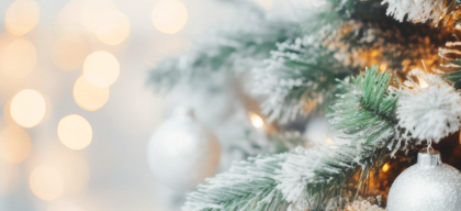 Ein Weihnachtsbaum ist mit silbernen Kugeln und einer Spur Schnee geschmückt, mit Bokeh-Lichtern im Hintergrund.