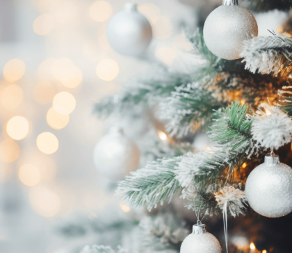 Ein Weihnachtsbaum ist mit silbernen Kugeln und einer Spur Schnee geschmückt, mit Bokeh-Lichtern im Hintergrund.