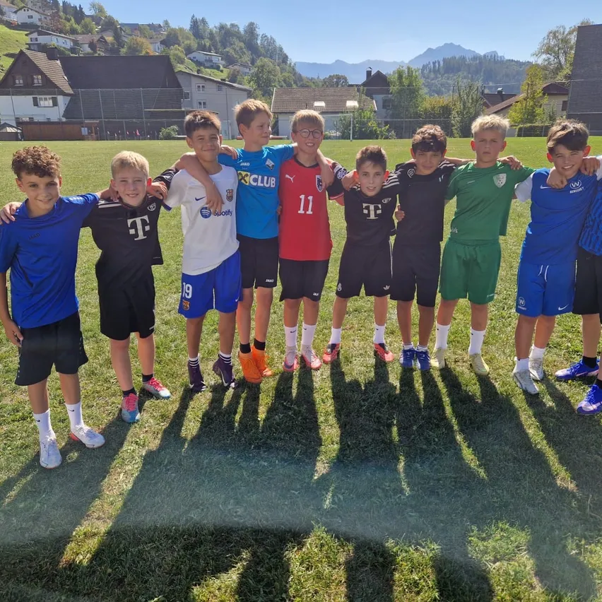 Eine Gruppe junger Jungen in verschiedenen farbigen Fußballtrikots steht zusammen auf einem Rasenfeld.