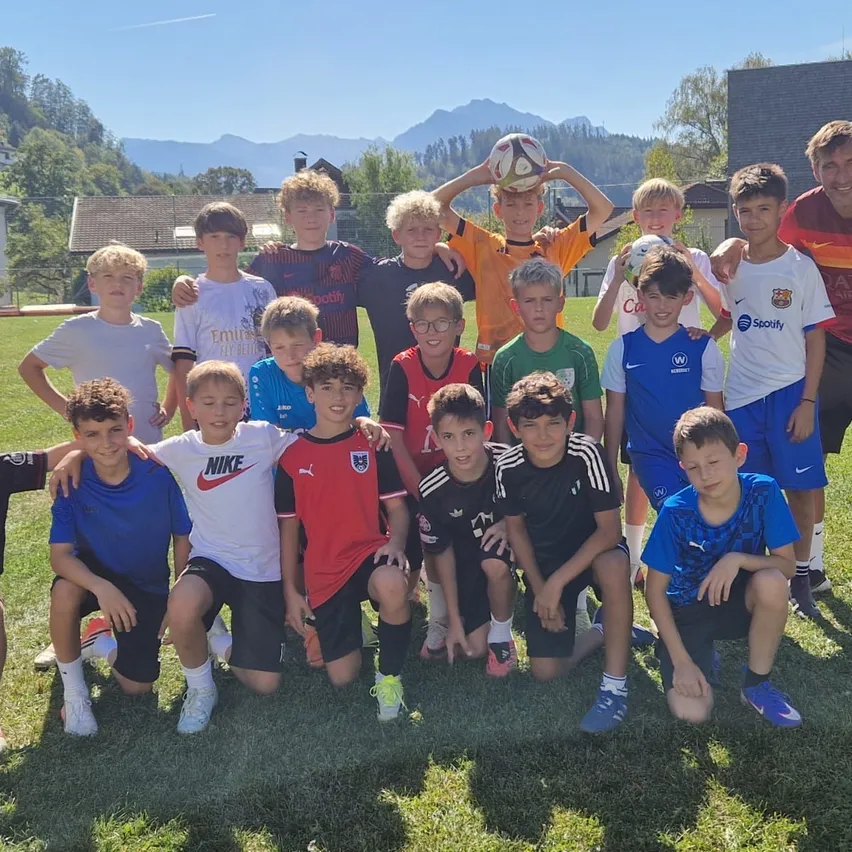Eine Gruppe junger Jungen und ein Mann posieren für ein Foto auf einem Fußballfeld. Die Jungen tragen verschiedenfarbige Trikots, und einer von ihnen hält einen Fußball.