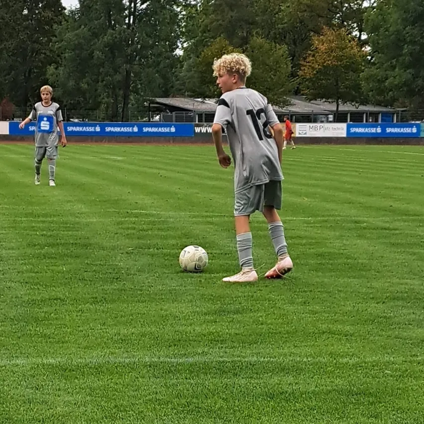 Zwei Jungen spielen Fußball auf einem grünen Feld. Ein Junge läuft auf den Ball zu, während der andere Junge ihn ansieht.