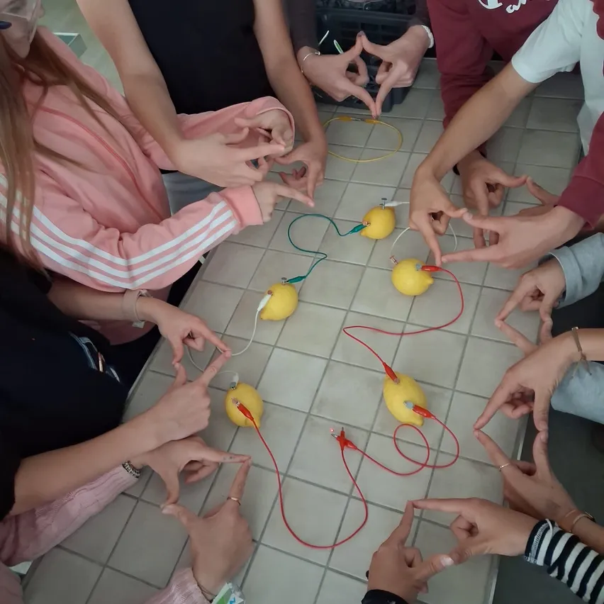 Eine Gruppe von Schülern führt ein Experiment mit Zitronen und Drähten auf einem gefliesten Tisch durch.