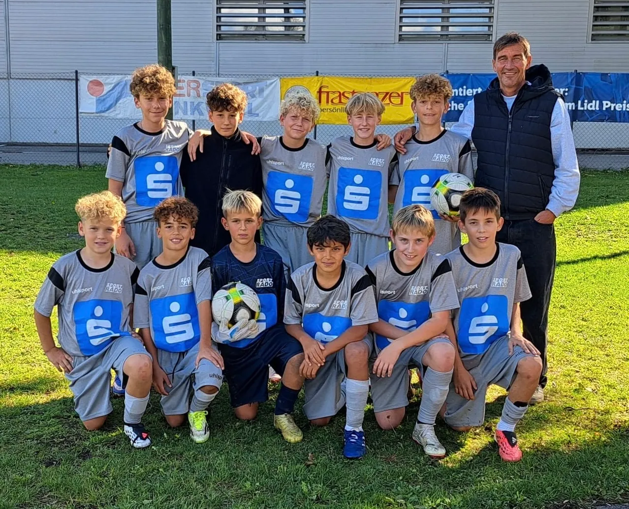 Eine Gruppe junger Jungen in Sportuniformen posiert für ein Teamfoto auf einem Rasenfeld.