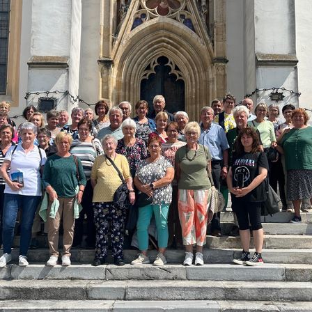 Eine Gruppe von Menschen, hauptsächlich älterer Menschen, steht auf den Stufen einer Kirche, lächelt und posiert für ein Foto.