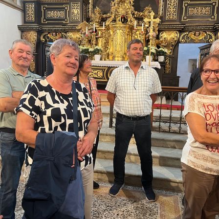 Eine Gruppe von Menschen steht vor einem golden verzierten Altar einer Kirche, lächelt und posiert für ein Foto.