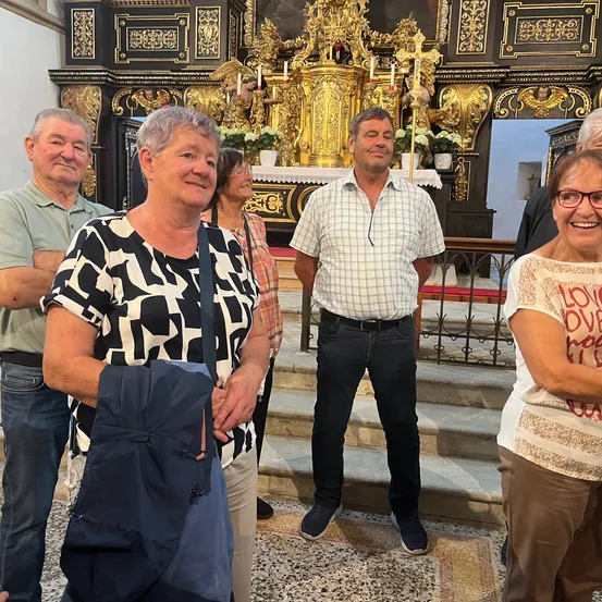Eine Gruppe von Menschen steht vor einem golden verzierten Altar einer Kirche, lächelt und posiert für ein Foto.