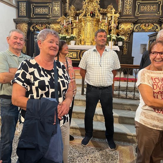 Eine Gruppe von Menschen steht vor einem golden verzierten Altar einer Kirche, lächelt und posiert für ein Foto.