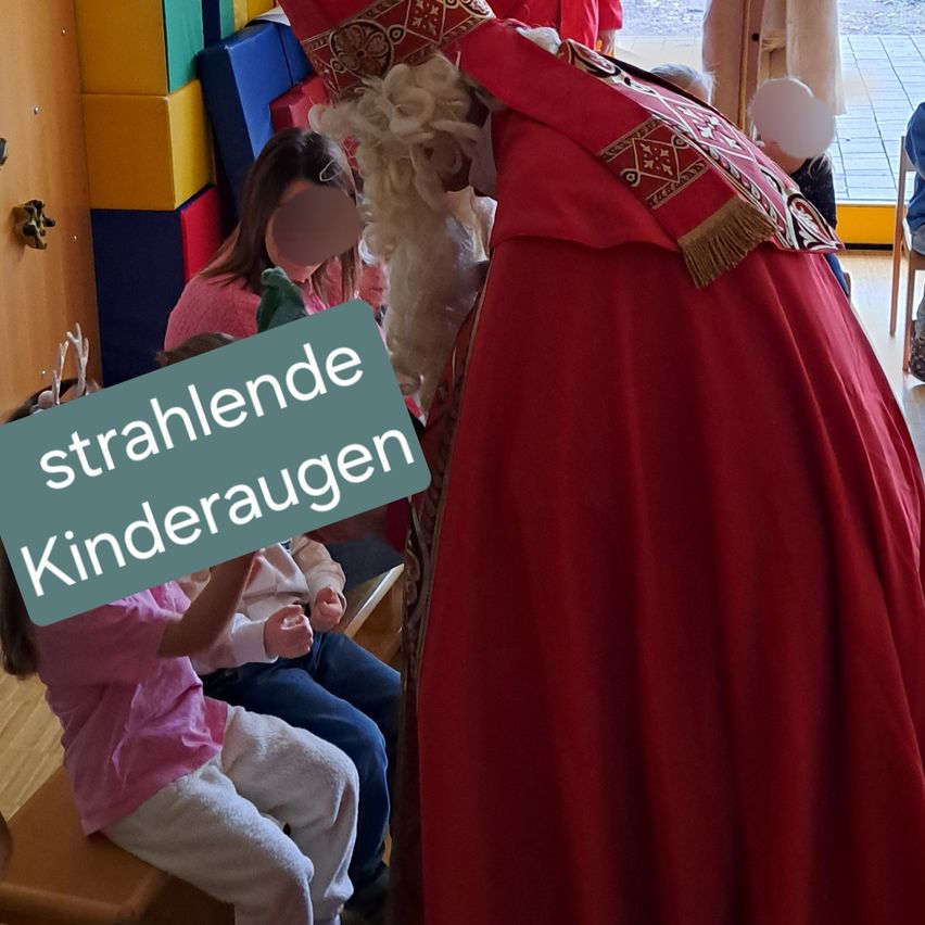 Ein Mann in einem roten Gewand mit goldenen Verzierungen spricht mit Kindern, die auf einer Bank sitzen. Der Text 'strahlende Kinderaugen' ist auf einem grünen Schild sichtbar.