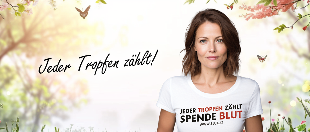 Eine Frau posiert für ein Foto in einem weißen T-Shirt mit der Aufschrift 'Jeder Tropfen zählt, spende Blut' mit einem unscharfen Hintergrund, der Schmetterlinge und Grünpflanzen zeigt.