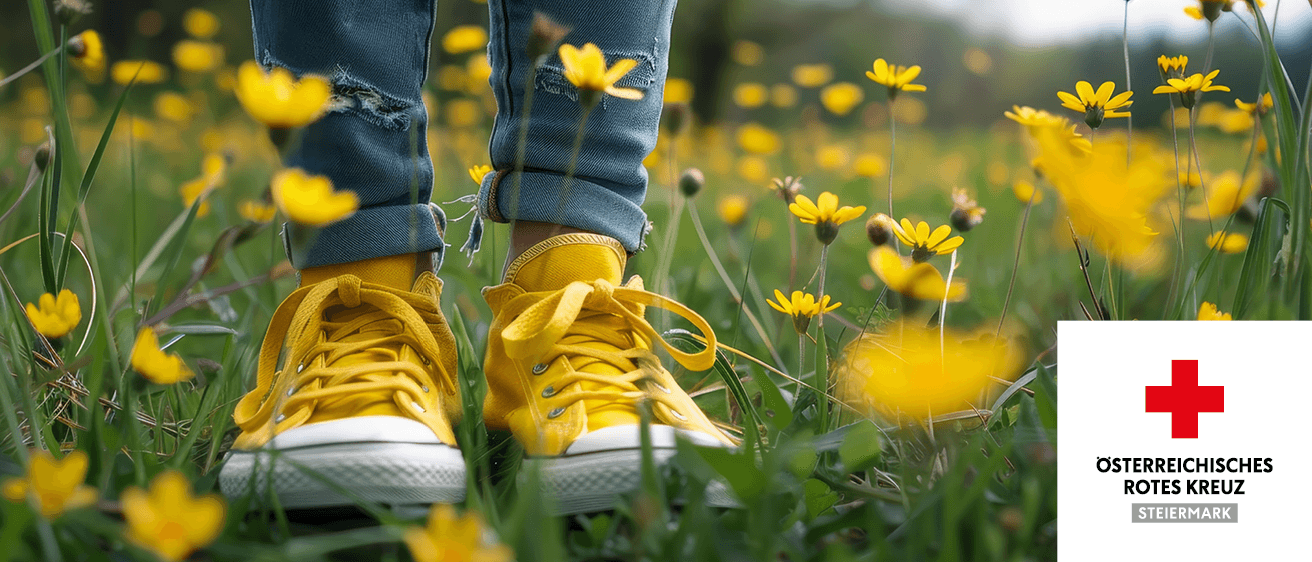 Eine Person in gelben Turnschuhen steht in einem Feld gelber Blumen. Die Jeans der Person hat Löcher.