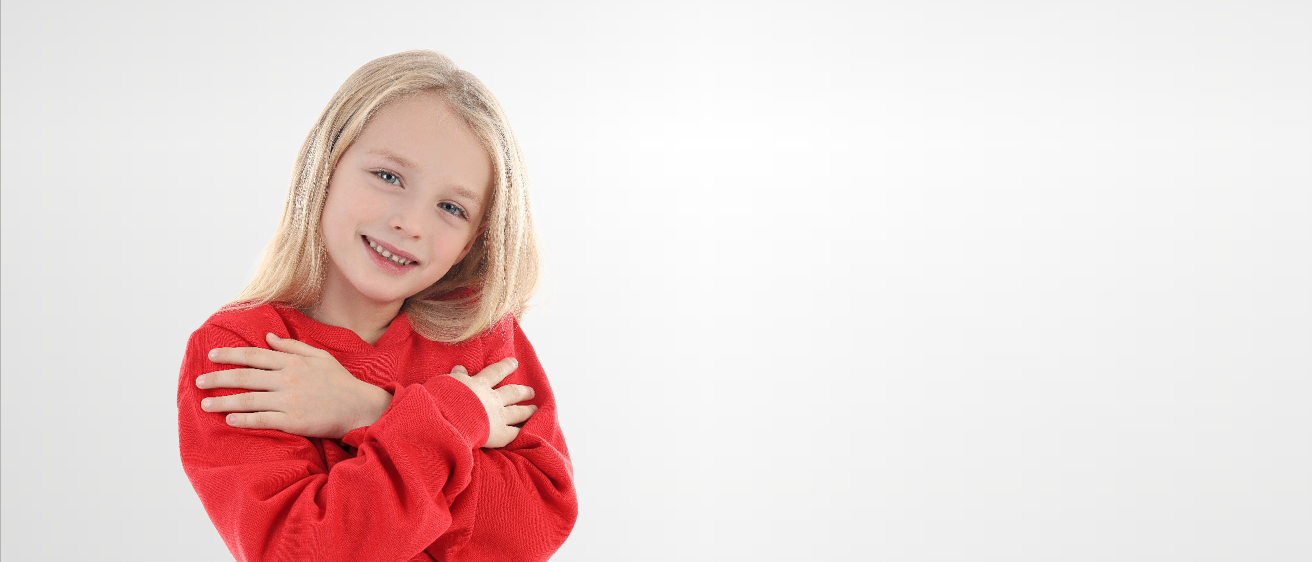 Ein lächelndes junges Mädchen mit blonden Haaren trägt einen roten Pullover und umarmt sich selbst. Sie hat die Augen geschlossen und posiert für ein Foto.