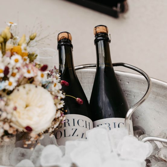Zwei Flaschen Wein mit Korken kühlen in einem Eiseimer mit Blumen an der Seite.