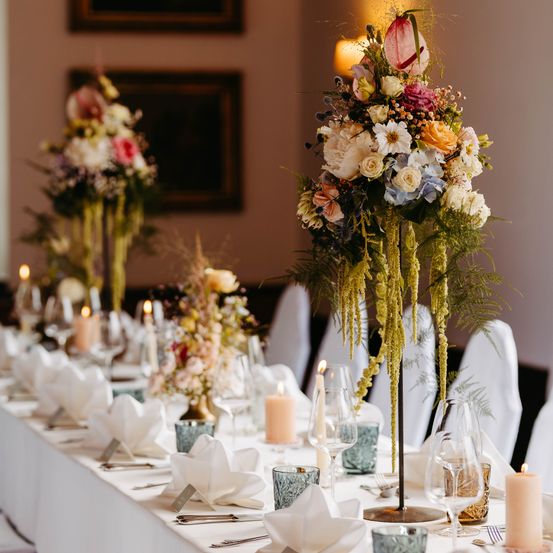 Ein wunderschön gedeckter Esstisch mit Blumenarrangements, Kerzen und gefalteten Servietten, die eine warme und einladende Atmosphäre schaffen.