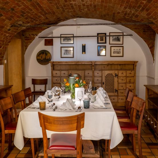 Ein Esszimmer mit gemauerten Bogendecken, Holzschränken und einem Tisch, der für eine Mahlzeit mit Blumen, Weingläsern und Besteck gedeckt ist.