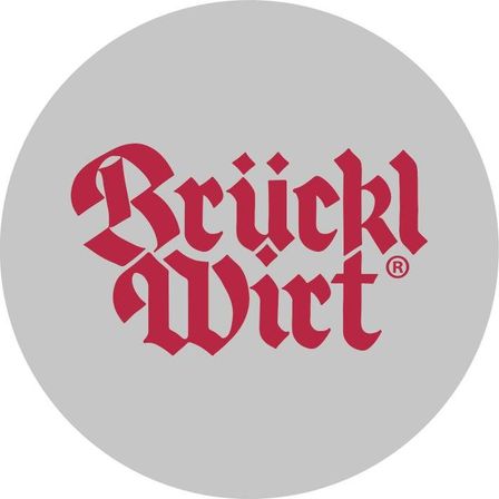 Ein kreisförmiges Logo mit dem Wort 'Bruckl' in roter gotischer Schrift und 'Wirt' darunter, alles auf einem grauen Hintergrund.