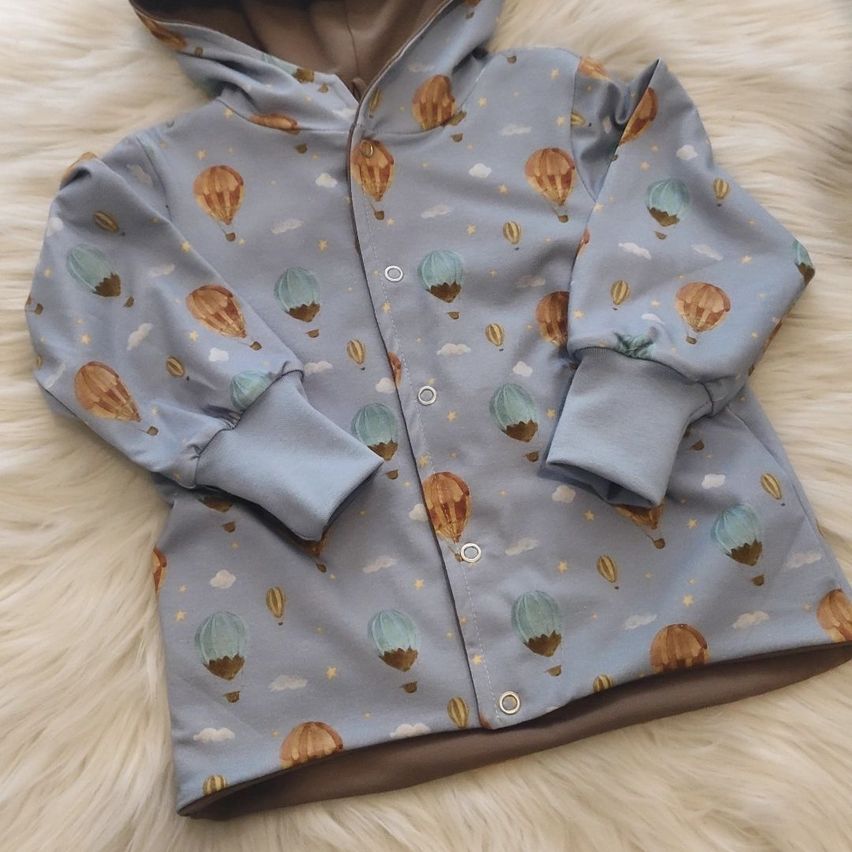 A blue hoodie jacket with a hot air balloon print on a white fur background.