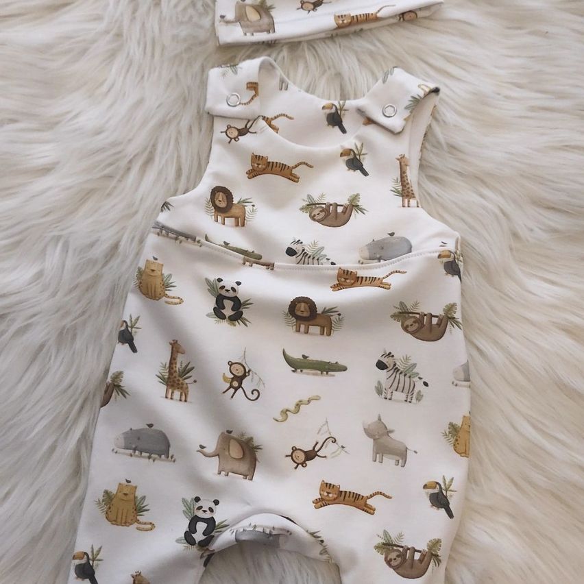 A white baby romper with various animals printed on it, including lions, tigers, elephants, and giraffes. It is laid on a white furry surface.