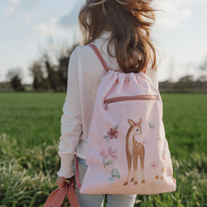 Ein Mädchen mit langen Haaren geht auf einem Feld mit einem rosa Rucksack, der einen Hirsch und Blumen zeigt.