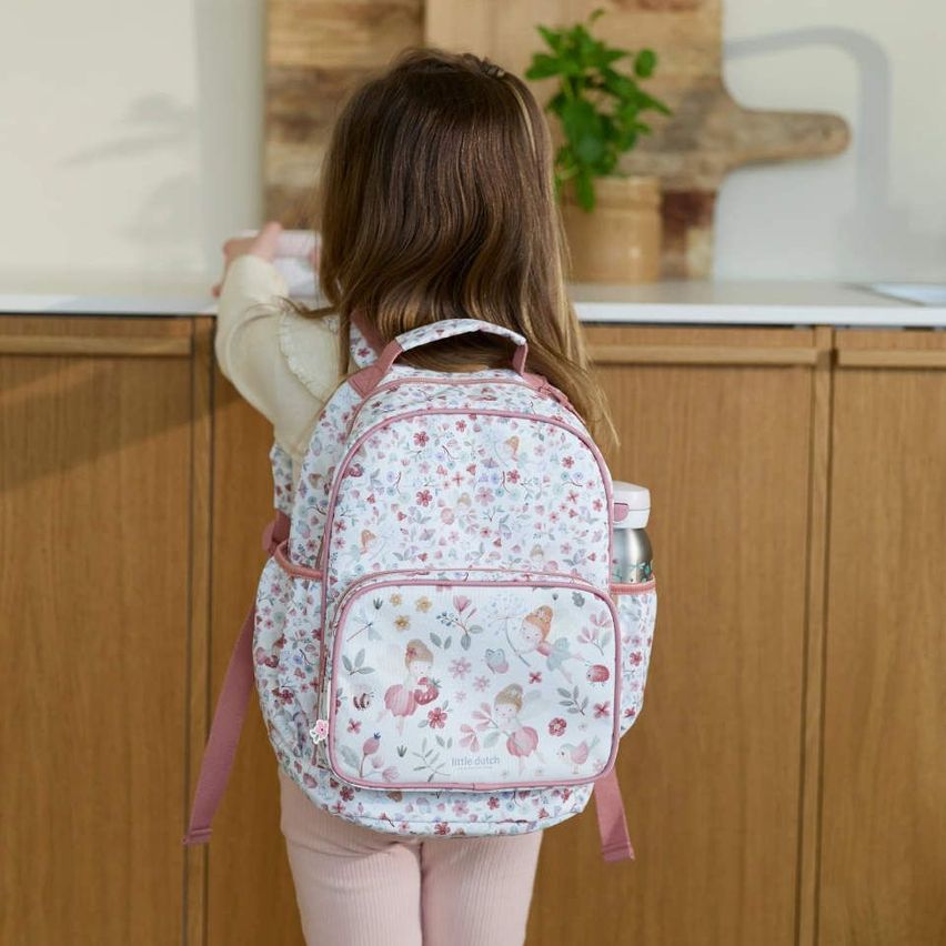 Ein kleines Mädchen mit einem rosa Rucksack mit Blumendesign steht vor einer hölzernen Küchentheke.