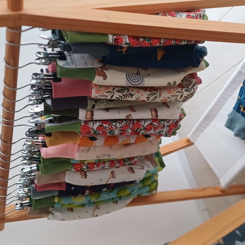 A wooden rack displays a colorful assortment of folded clothes, each with unique floral and fruit designs.