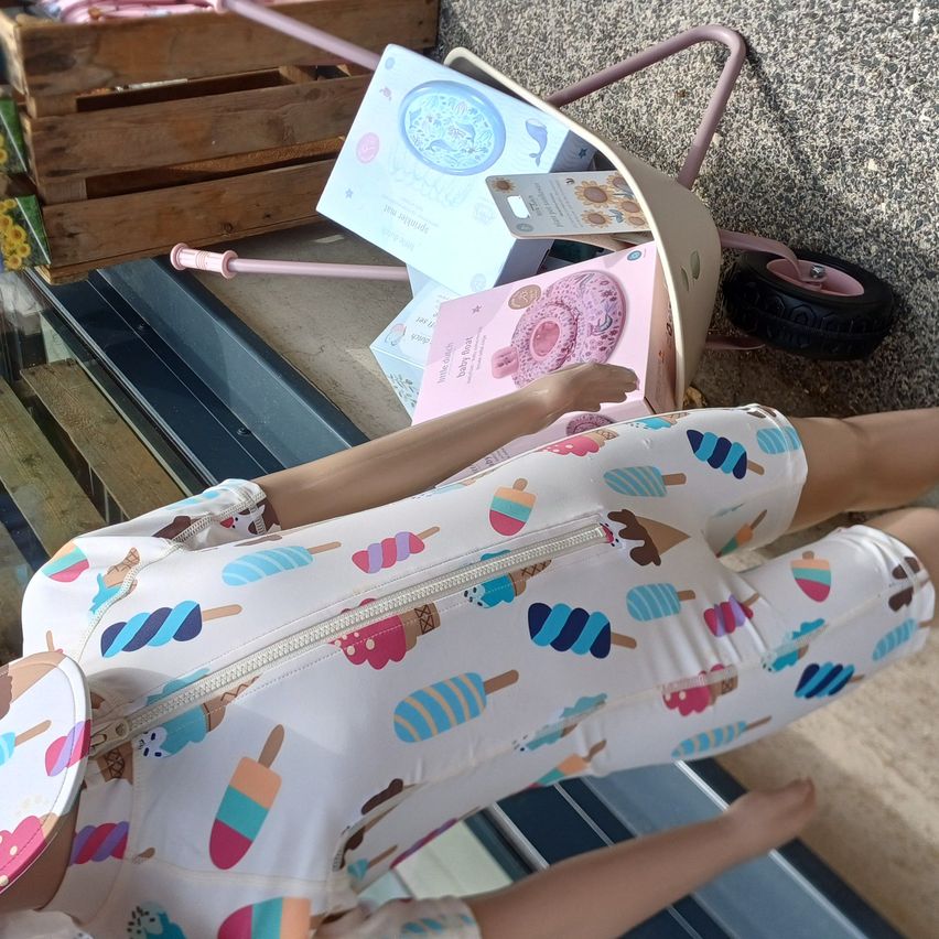A doll dressed in ice cream-themed pajamas lies on the floor with a pink wheelbarrow and gift boxes nearby.