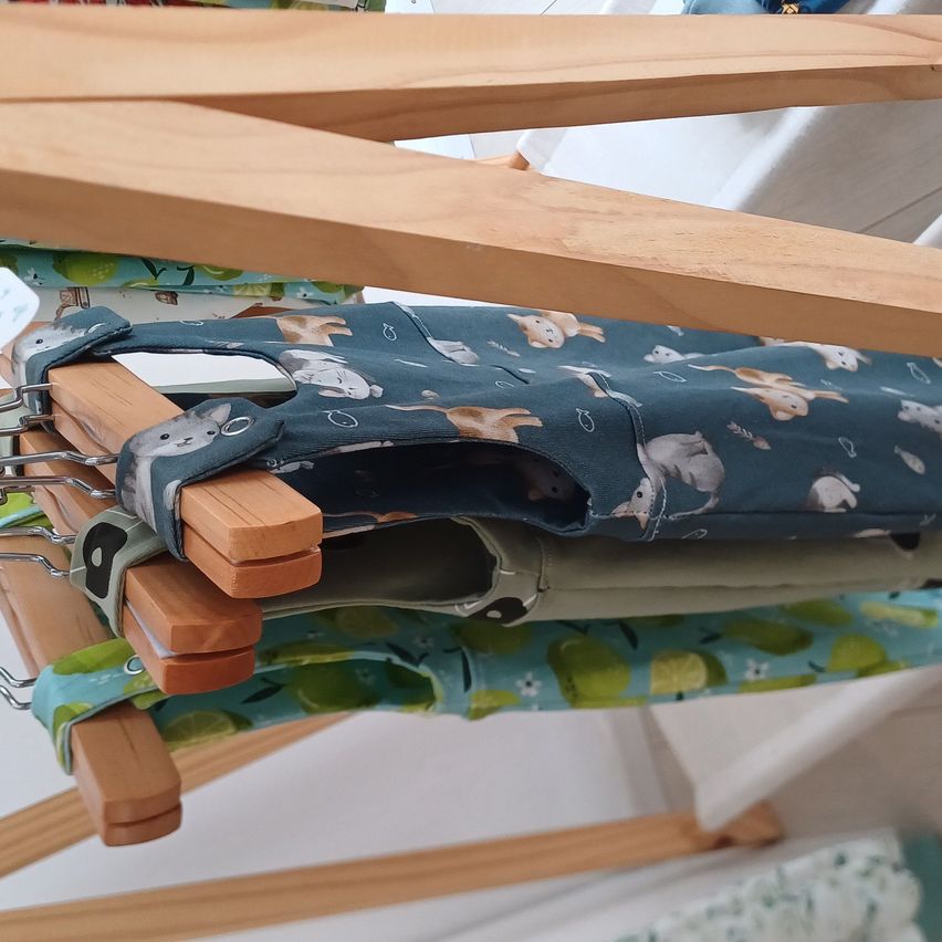 A close-up view of wooden hangers holding baby clothes with animal prints, including cats and mice, on a white background.