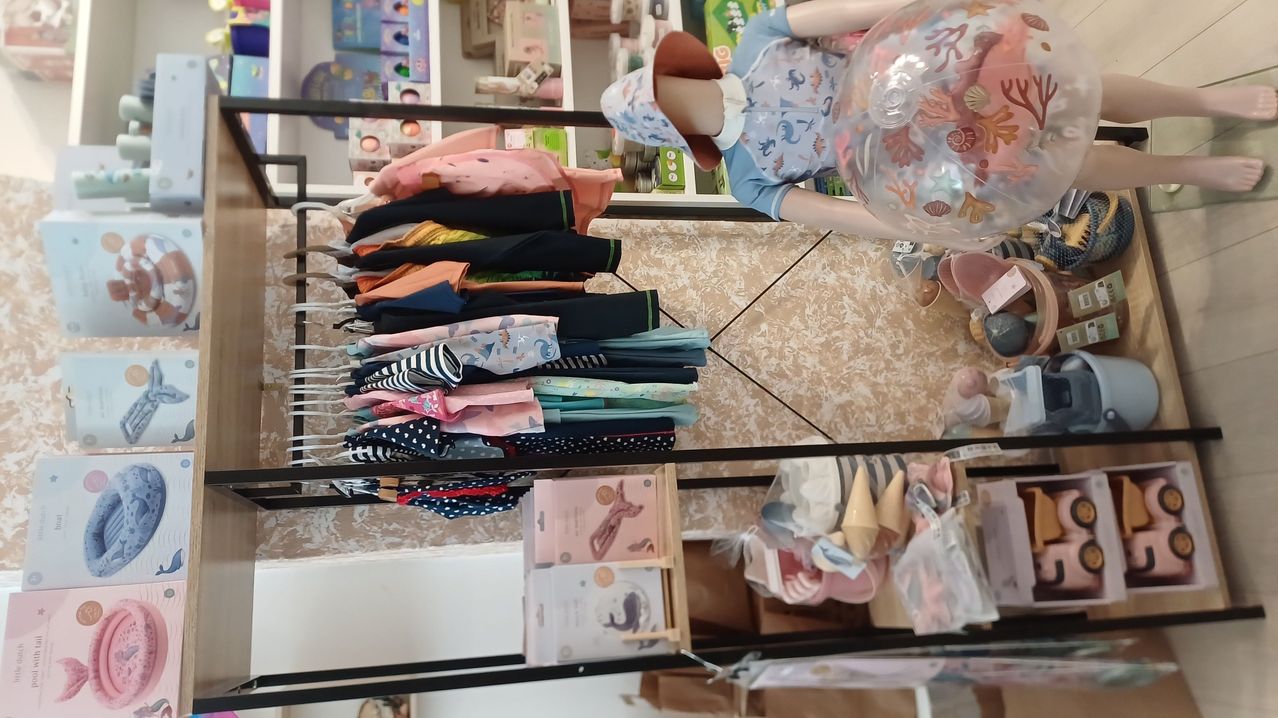 A store display with a mannequin wearing a hat and holding a balloon, surrounded by various children's clothing items on hangers and shelves.