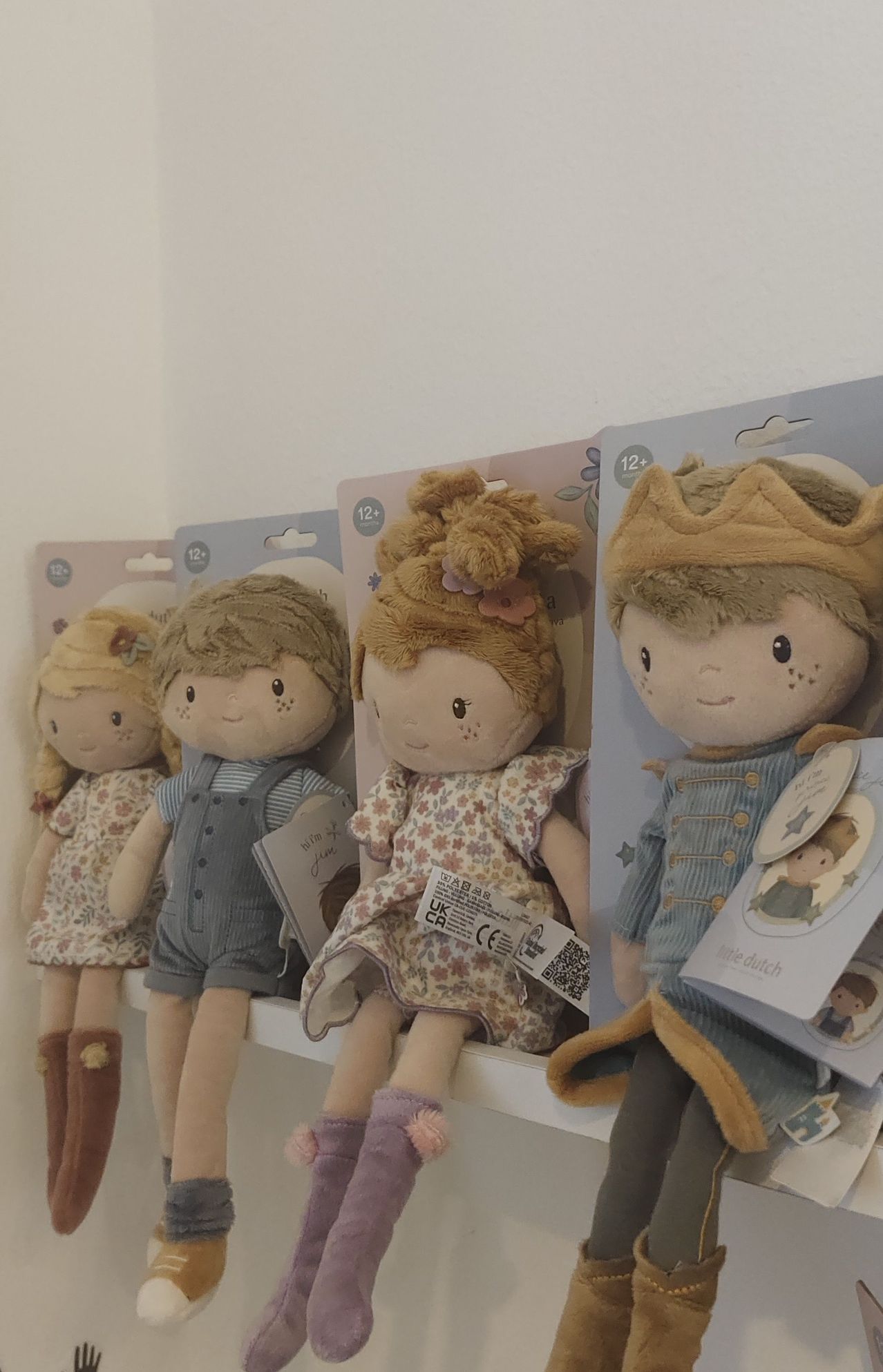 Four plush toys in boxes, each with different outfits and accessories, displayed on a white shelf.