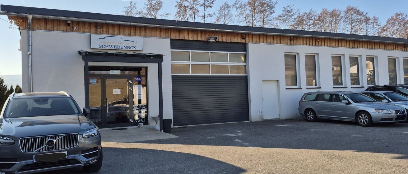 Ein Parkplatz vor einem Gebäude mit dem Namen Schwedenbox. Vor dem Gebäude sind zwei Autos geparkt.