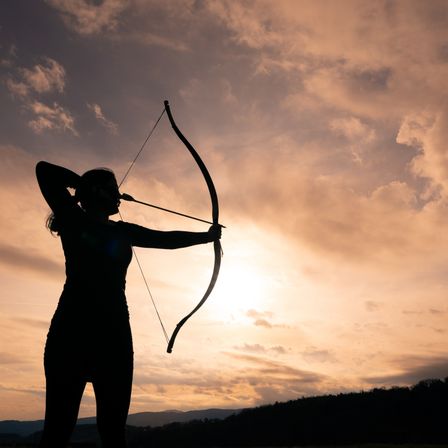 Eine Silhouette einer Frau mit Bogen und Pfeil steht vor einem Sonnenuntergangshimmel.