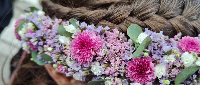 Ein Mädchen mit geflochtenem Haar trägt eine Blumenkrone mit lila und rosa Blumen und schaut nach vorne.