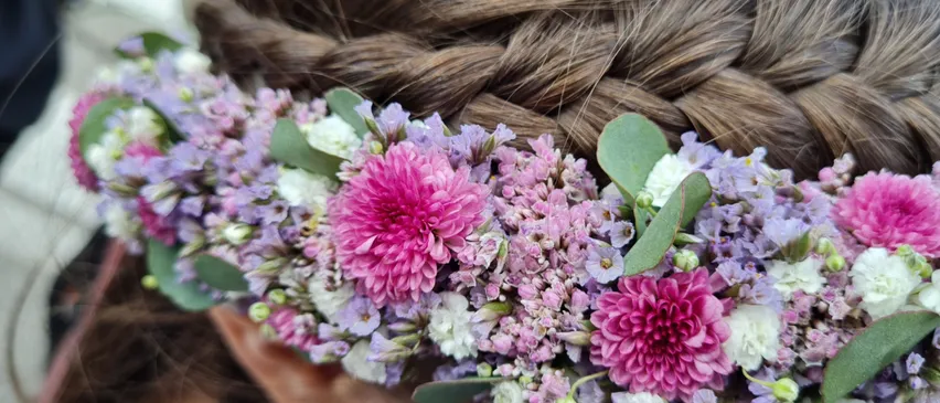 Ein Mädchen mit einer geflochtenen Frisur, geschmückt mit einer Blumenkrone aus rosa, lila und weißen Blumen.
