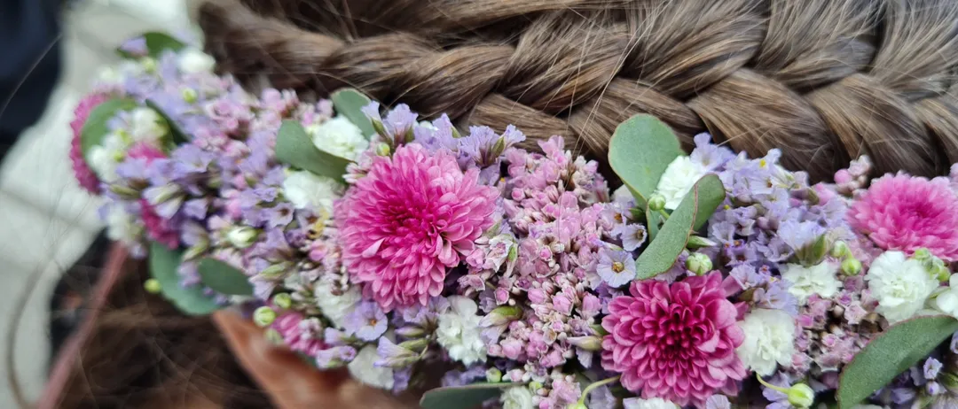 Ein Mädchen mit einer geflochtenen Frisur, geschmückt mit einer Blumenkrone aus rosa, lila und weißen Blumen.