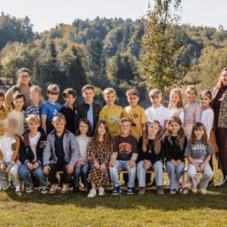 Eine Gruppe junger Schüler und zwei Lehrer posieren für ein Foto in einem Park mit grünem Rasen und Bäumen.