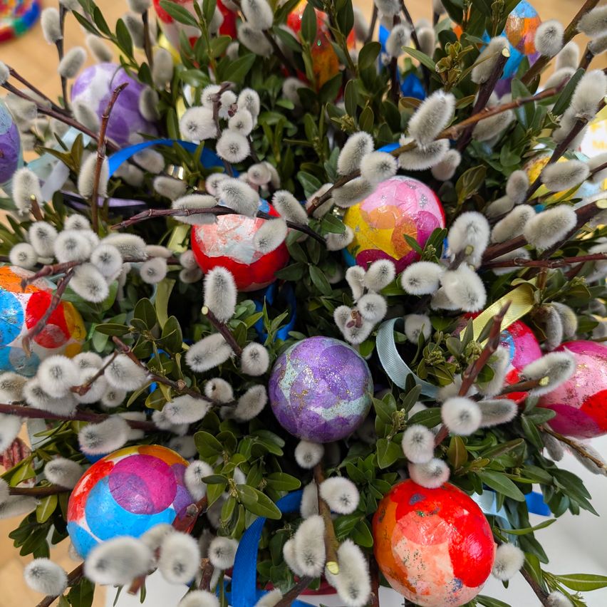 Ein Nahaufnahme einer bunten Ostereier-Arrangement mit vielfarbigen Eiern, zarten weißen Zweigen und flauschigen Baumwollbügeln auf weißem Hintergrund.