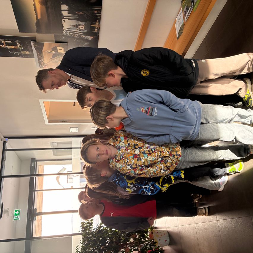 Eine Gruppe von Kindern und Erwachsenen steht zusammen in einem Gebäude. Sie posieren für ein Foto mit einem lächelnden Mann hinter ihnen.