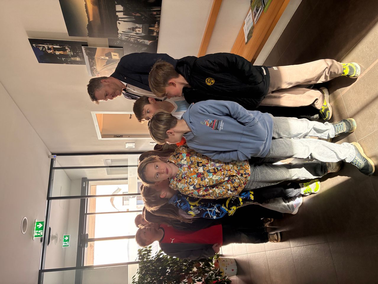 Eine Gruppe von Kindern und Erwachsenen steht zusammen in einem Gebäude. Sie posieren für ein Foto mit einem lächelnden Mann hinter ihnen.