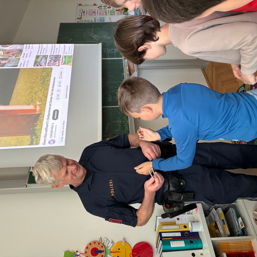 Ein Feuerwehrmann demonstriert Sicherheitstipps für Schüler in einem Klassenzimmer. Die Kinder sehen aufmerksam zu.