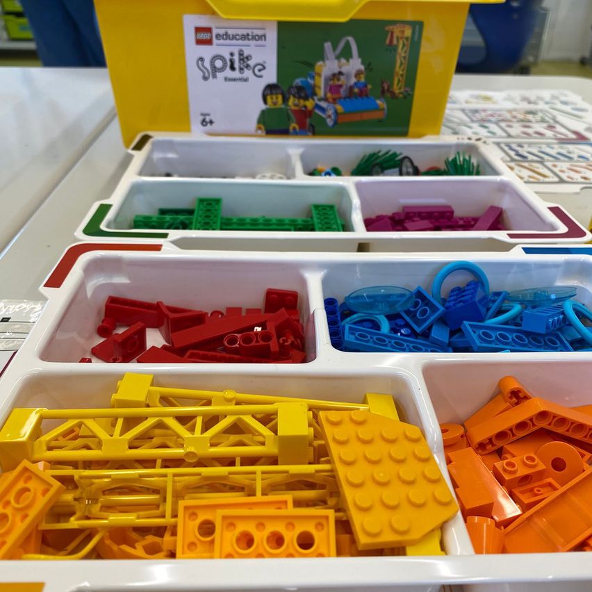 Eine Vielzahl von LEGO Education Spike Essential-Stücken in verschiedenen Farben und Größen sind in getrennten Behältern auf einem Tisch ausgestellt.