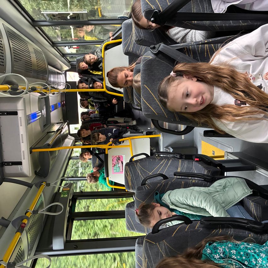 Kinder auf einem Bus, einige schlafen und andere sind wach. Ein Mädchen mit langen Haaren lächelt in die Kamera.