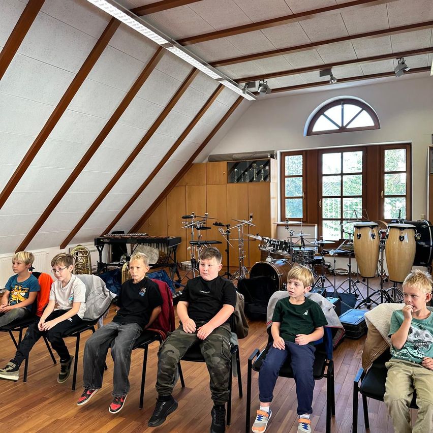 Eine Gruppe junger Jungen sitzt in Stühlen in einem Musikraum mit verschiedenen Musikinstrumenten um sie herum.
