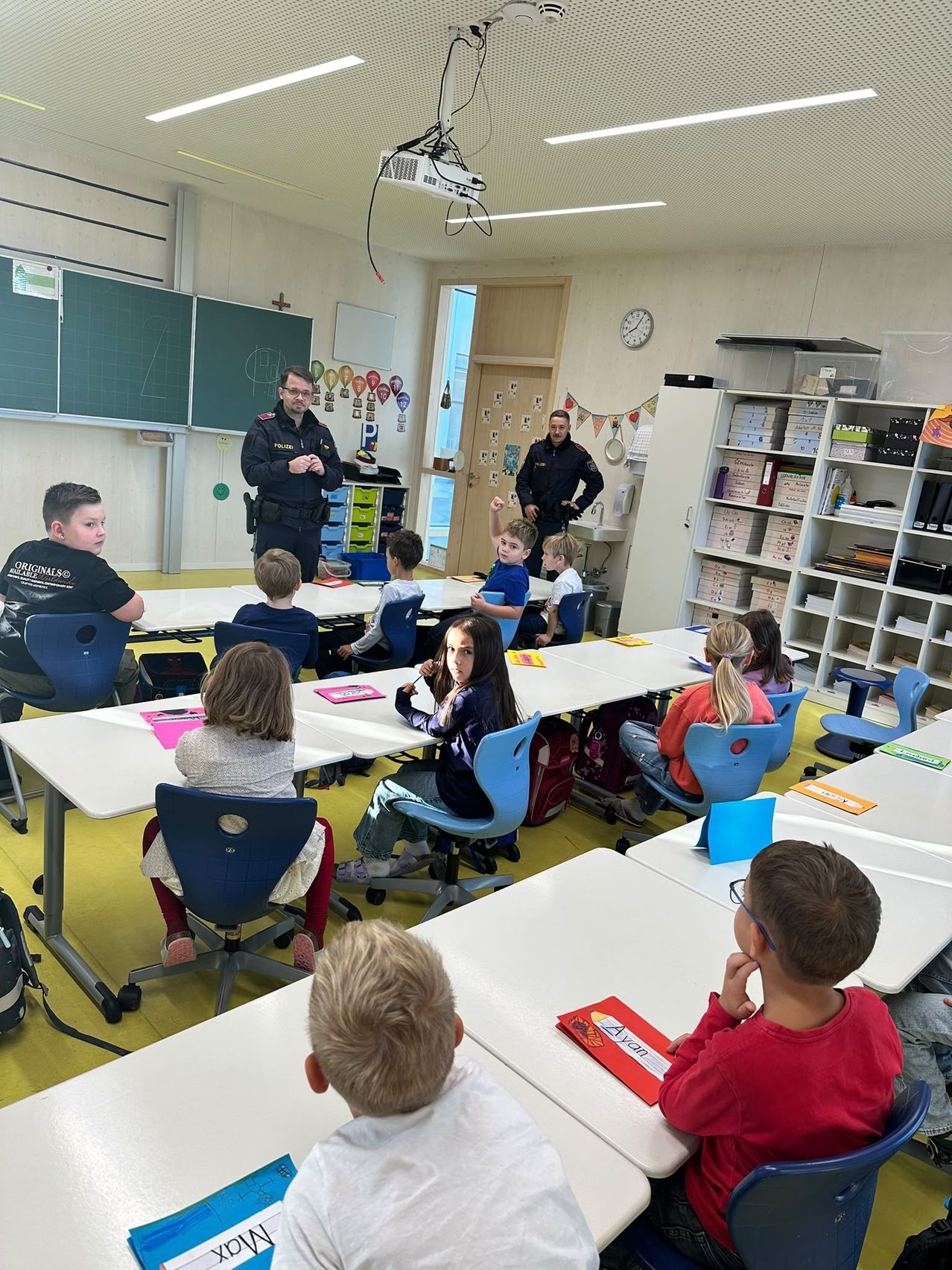 Ein Klassenzimmer mit Schülern und zwei Polizeibeamten. Die Beamten stehen vorne, und die Schüler sitzen an ihren Tischen.
